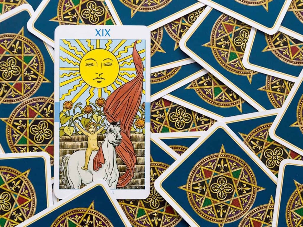 Büyük bir tarot kartı olan güneş kartı ön planda, arka planda ise benzer desenlere sahip kartlar dağınık halde yer alıyor. Güneş kartı, parlak ve dikkat çekici.